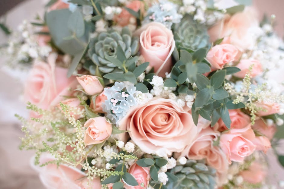 A close-up view of a floral arrangement featuring fresh, soft pink roses and pale peach roses in full bloom, complemented by clusters of small white baby's breath and silvery-green eucalyptus leaves. 